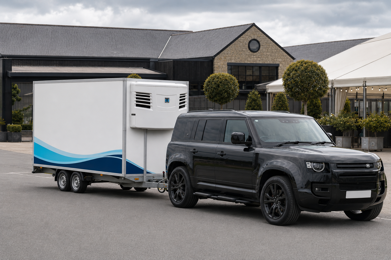 Black Defender towing a blue-wrapped refrigerated trailer